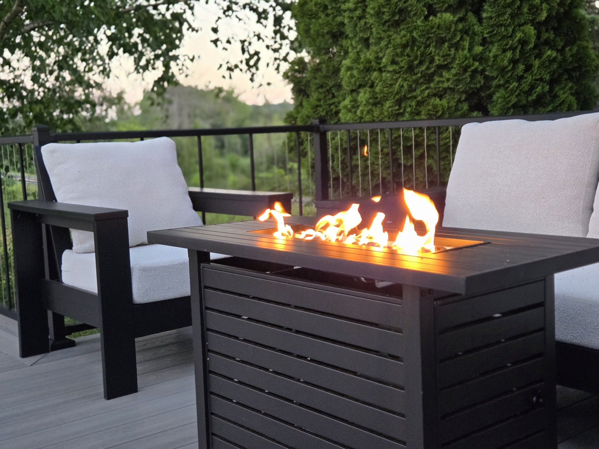 Gas fire table lit at dusk on the deck, flanked by cushioned patio chairs
